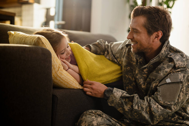 Caring military dad tucking his sleepy daughter in the living room.  - Zdjęcie, obraz