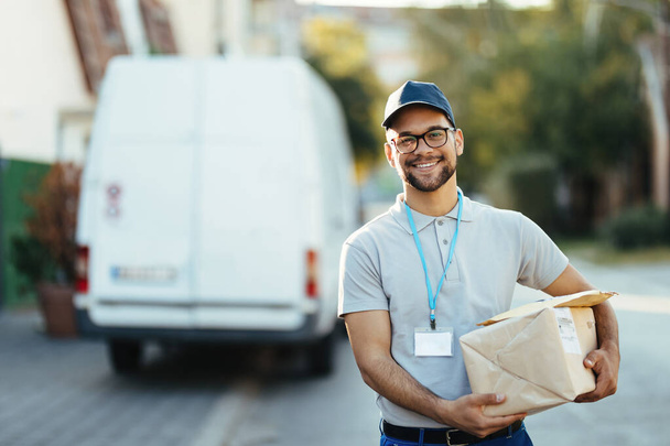 Portrait of happy delivery man carrying packages and looking at camera while standing on the street.  - Foto, Imagen