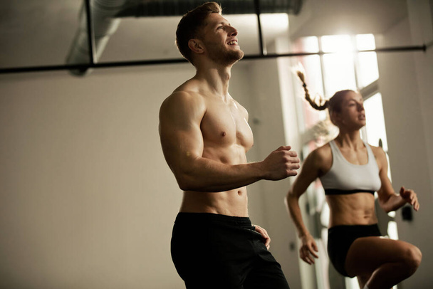 Young athletic couple having sports training in a gym and warming up. Focus is on man.  - Photo, image
