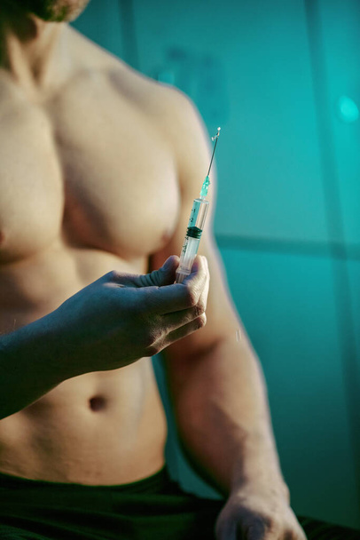 Close up of muscular build man with injection of anabolic steroids in gym's changing room.  - Foto, immagini