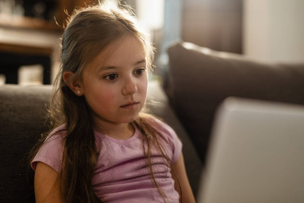 Задумчивая маленькая девочка, сидящая дома в интернете.  - Фото, изображение