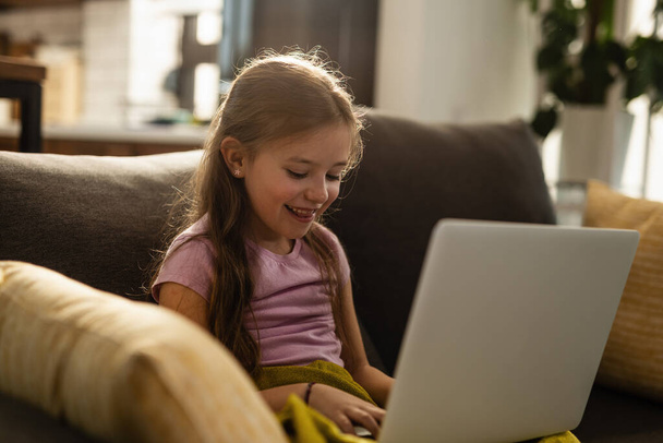Щаслива маленька дівчинка розслабляється у вітальні та серфінгує мережу на комп'ютері
.  - Фото, зображення
