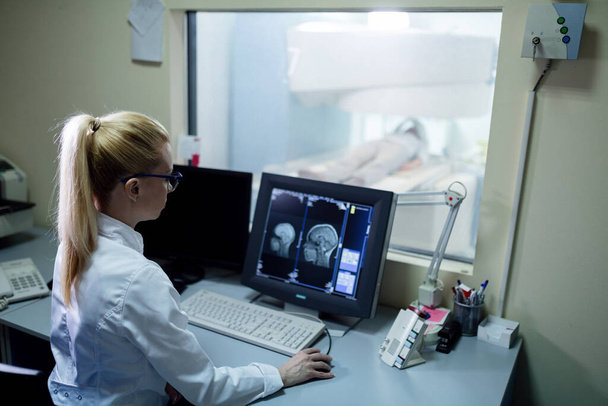 Radiologist analyzing brain MRI scan results of a patient on computer monitor in control room.  - 写真・画像