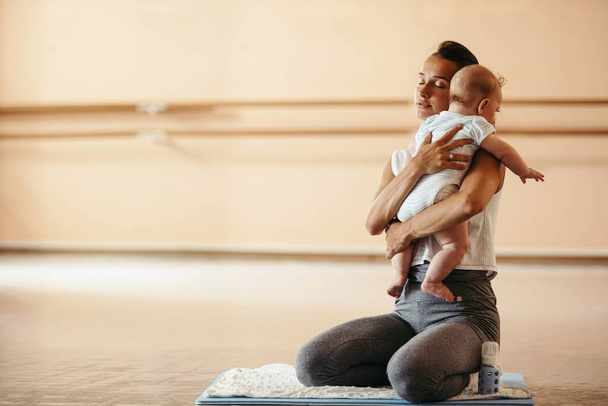 Athletic mother consoling her crying baby while exercising in a health club. Copy space.  - Fotoğraf, Görsel