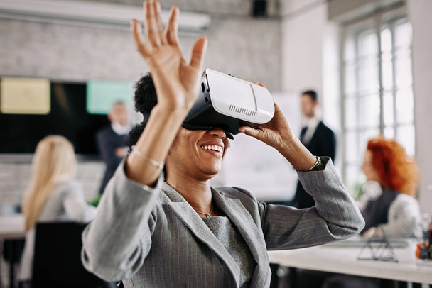 Афроамериканська бізнес-леді, яка розважається з віртуальною реальністю окуляри в офісі.  - Фото, зображення