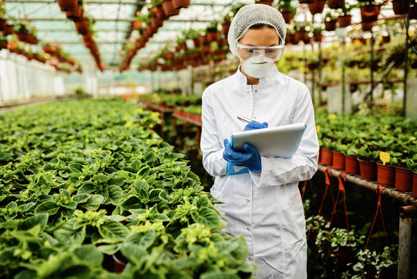 Female scientist inspecting growth of potted flowers and taking notes in a greenhouse.  - Foto, Bild