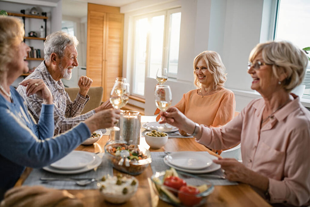 Happy senior friends having lunch together and toasting with wine at dining table.  - Foto, imagen