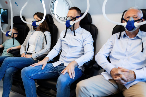 Небольшая группа людей, дышащих через маски во время гипербарической кислородной терапии в клинике. Внимание сосредоточено на мужчине средних лет.  - Фото, изображение