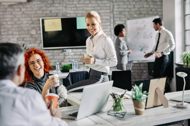 Group of business colleagues talking to each other while taking a break from work and drinking coffee in modern office. There are people in the background.  - 写真・画像