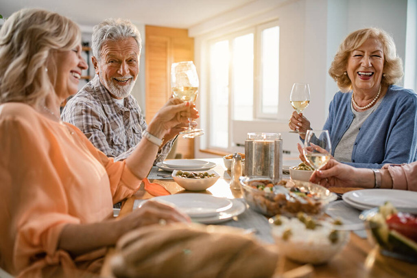 Happy seniors friends having lunch together and toasting with wineglasses at dining table at home.  - Foto, imagen