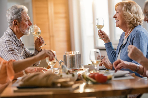 Ευτυχισμένο ώριμο ζευγάρι γευματίζει με φίλους και επικοινωνεί πίνοντας κρασί στο σπίτι. - Φωτογραφία, εικόνα
