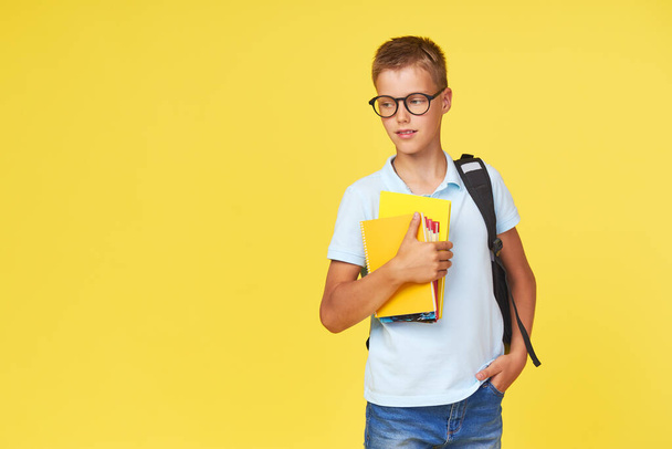 Портрет школьника в очках с учебниками и рюкзаком на жёлтом фоне. Возвращение в школу - Фото, изображение
