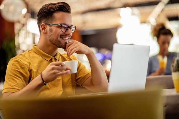 Счастливчик, сидящий в сети за компьютером и пьющий кофе в баре.  - Фото, изображение