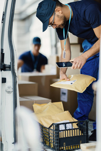 Delivery man preparing package for shipment and scanning bar code on a label with digital tablet in a van.  - Foto, Bild