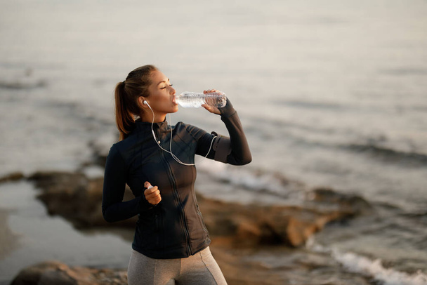Young sportswoman with eyes closed refreshing herself with water while exercising at the beach. Copy space.  - Foto, Bild