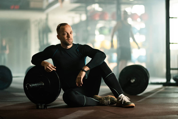 Muscular build man resting after cross training with barbell in a health club. - Φωτογραφία, εικόνα