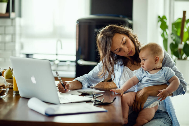 Young working mother planning home budget while being with her baby at home.  - Fotoğraf, Görsel