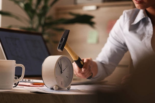 Unrecognizable businesswoman using hammer and about to smash clock on her office desk.  - Foto, Bild