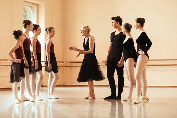 Happy female ballet instructor communicating with group of ballet dancer before the rehearsal at dance studio.  - Foto, imagen