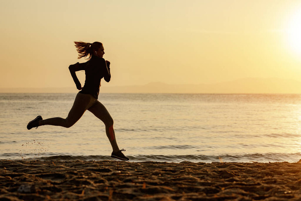 Full length of motivated athletic woman running at the beach at sunset. Copy space.  - Fotoğraf, Görsel