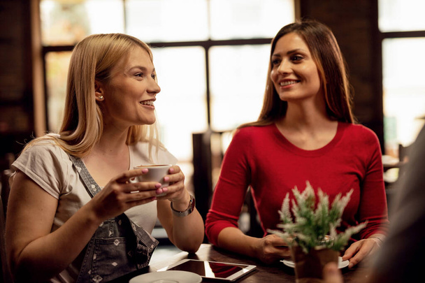 Νεαρή ευτυχισμένη γυναίκα διασκεδάζει περνώντας χρόνο με φίλους και πίνοντας καφέ σε ένα καφέ. - Φωτογραφία, εικόνα