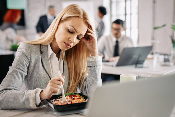 Pensive businesswoman eating vegetable salad during her lunch break in the office.  - Foto, Bild