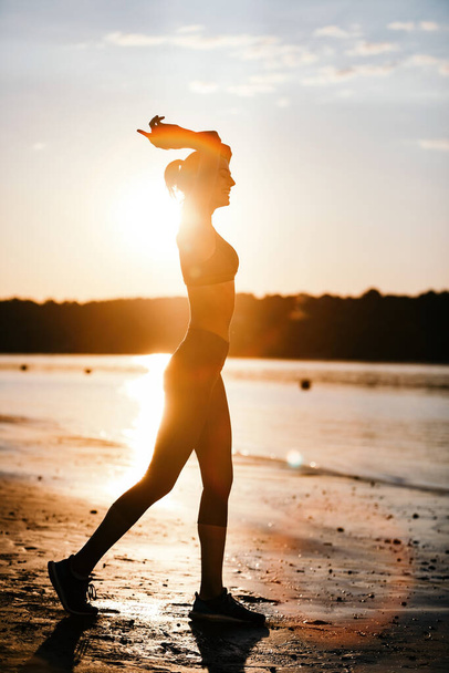 Full length of happy athletic woman enjoying at sunrise at riverside.  - Zdjęcie, obraz