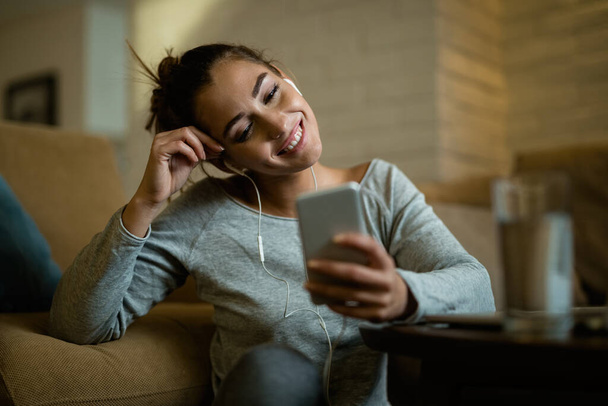 Young happy woman enjoying in the evening while using smart phone in the living room.  - Foto, Imagen
