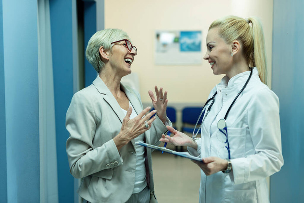 Happy female doctor and mature woman talking while going through medical reports at clinic.  - Foto, imagen