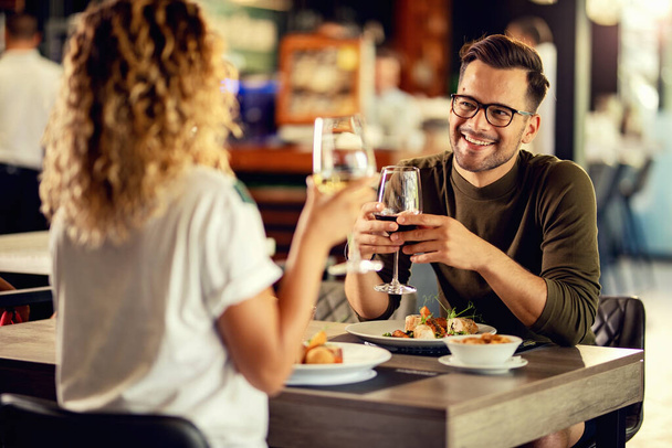 Young happy man communicating with his girlfriend while having a lunch and drinking wine in a restaurant.  - Zdjęcie, obraz