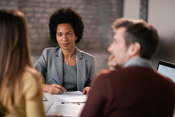 Черная женщина-менеджер банка проводит деловую встречу с парой слушающих их требования по кредитам. - Фото, изображение
