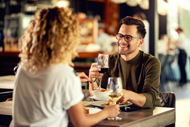 Молодой счастливый человек разговаривает со своей девушкой, выпивая вино и обедая в ресторане.  - Фото, изображение