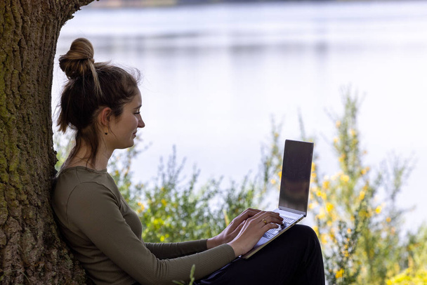 Work from anywhere. Remote freelancer work in nature using renewable energy via a foldable solar panel. Young woman, female freelancer working with laptop with Beautiful view of forest and lake - Foto, Bild