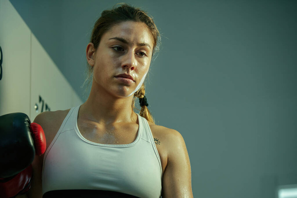 Низкий угол обзора потной спортивной женщины, созерцающей в раздевалке после тренировки по боксу. - Фото, изображение