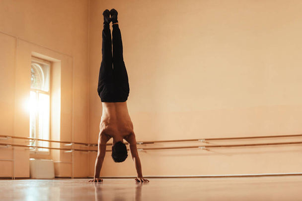Back view of male ballet dancer doing handstand while exercising in ballet studio. Copy space.  - Foto, afbeelding