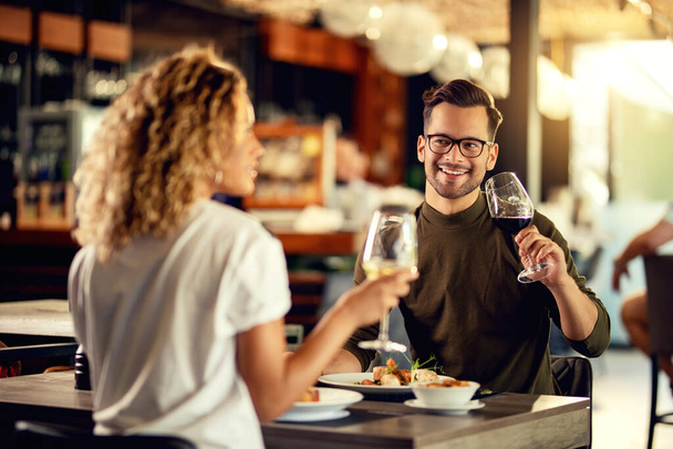 Happy couple enjoying in conversation while drinking wine and eating in a bar.  - 写真・画像