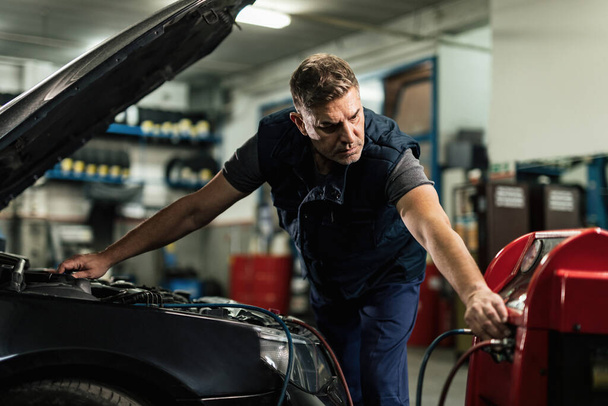 Mid adult mechanic doing service of car's air conditioner unit in auto repair shop.  - Foto, imagen