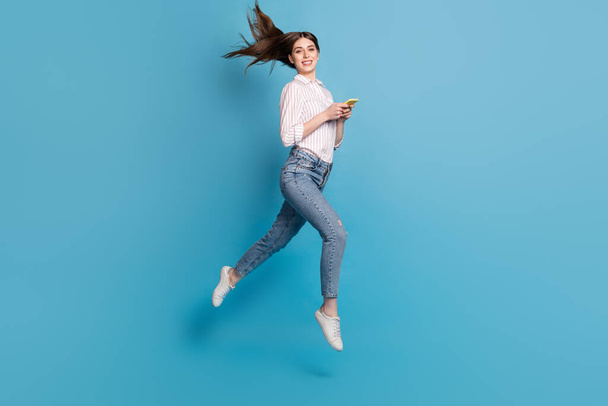 Full length body size view of attractive girl using gadget jumping fast speed isolated over bright blue color background. - Foto, immagini