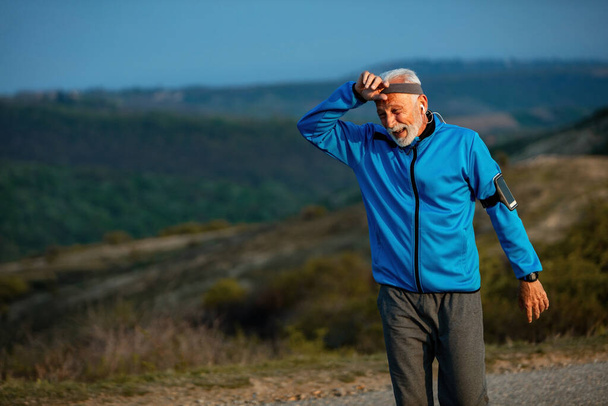 Mature athletic man feeling exhausted after jogging in the morning in nature. Copy space.  - Fotoğraf, Görsel