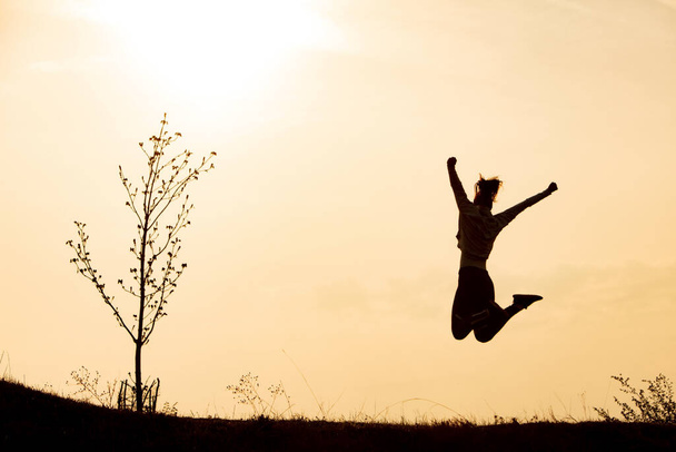 Вид спереду спортсменки, яка святкує успіх і стрибає зі зброєю, піднятою на полі під час сходу сонця. Копіювати простір
.  - Фото, зображення
