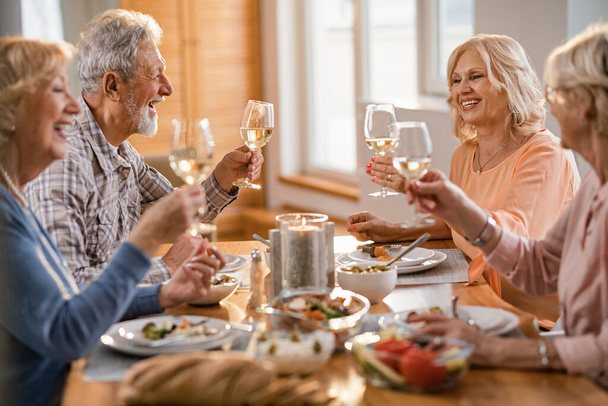 Group of happy senior friends having fun while toasting with wine during lunch time at dining table.  - 写真・画像