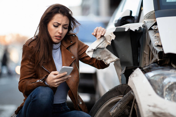Displeased woman using cell phone and texting after a car accident in the city.  - Photo, Image
