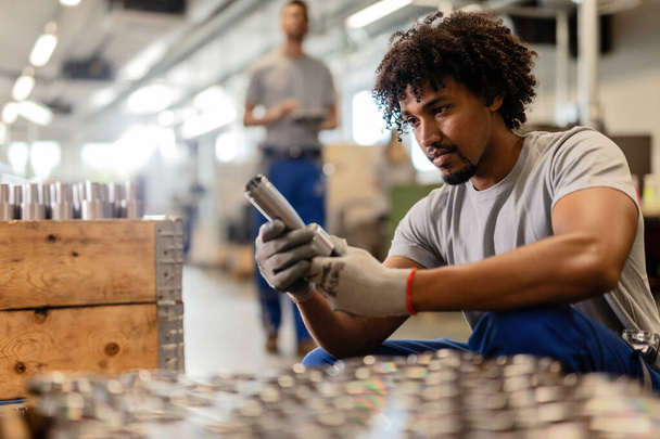 Young African American steel worker analyzing finished product in industrial building.  - Foto, Bild