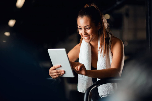 Счастливая спортсменка делает свой план упражнений на цифровом планшете во время занятий спортом в фитнес-центре.  - Фото, изображение
