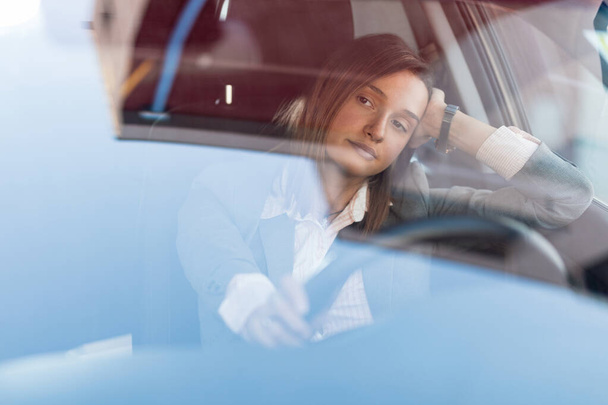 Young businesswoman driving a car and feeling bored while being stuck in traffic jam. The view is through the glass.  - Photo, Image