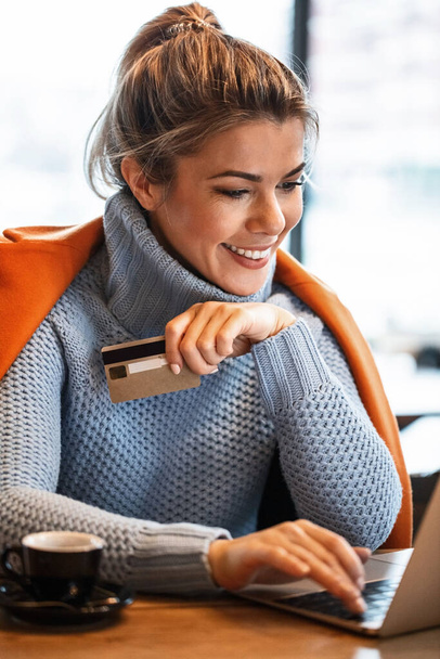 Νεαρή χαρούμενη επιχειρηματίας που χρησιμοποιεί πιστωτική κάρτα ενώ σερφάρει στο διαδίκτυο στο laptop και ψωνίζει online.  - Φωτογραφία, εικόνα