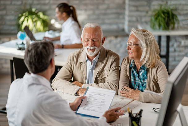 Happy senior couple communicating with a doctor about their health insurance while going through paperwork.  - Foto, Imagen