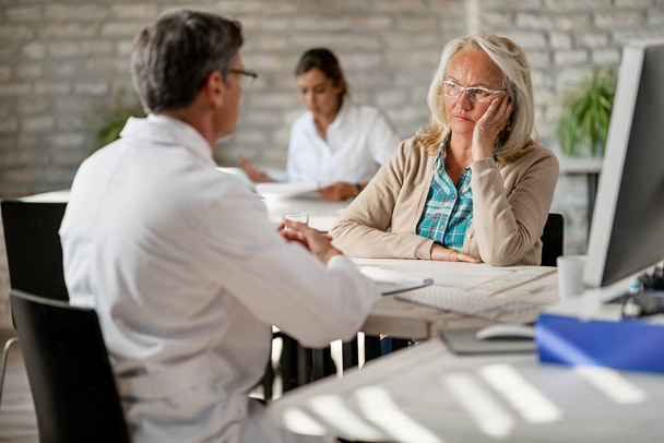 Занепокоєна зріла жінка розмовляє з медичним працівником про медичне страхування під час консультування в клініці
.  - Фото, зображення