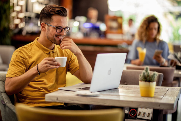 Ευτυχισμένος άνθρωπος χαλαρώνοντας σε ένα καφέ και σερφάροντας στο διαδίκτυο σε έναν υπολογιστή, ενώ πίνοντας καφέ.  - Φωτογραφία, εικόνα