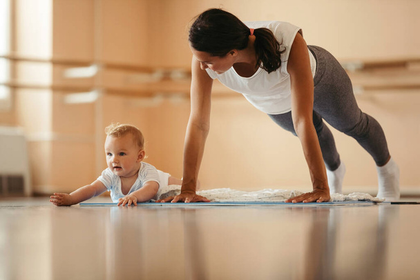 Young mother exercising push-ups while being on sports training with her baby. Copy space.  - Photo, Image
